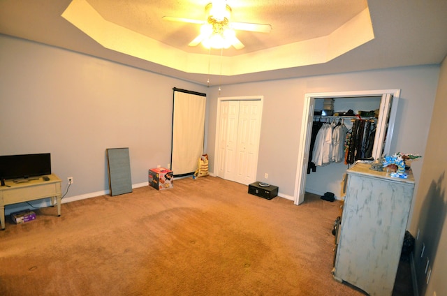 carpeted bedroom featuring multiple closets, ceiling fan, and a tray ceiling