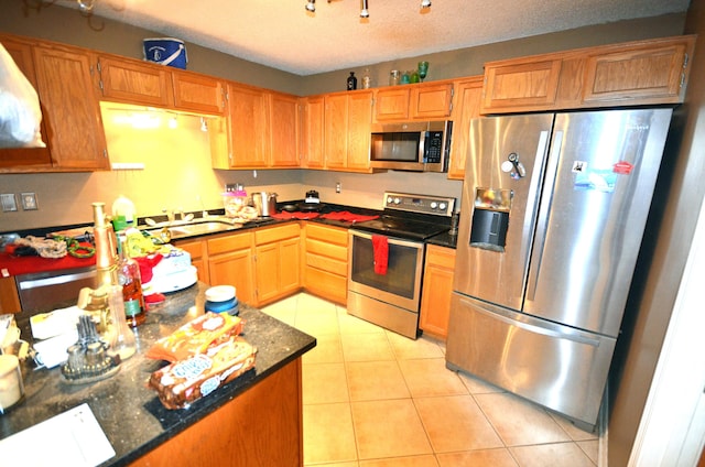 kitchen featuring light tile patterned floors, sink, appliances with stainless steel finishes, dark stone countertops, and a textured ceiling