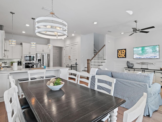 dining room featuring ornamental molding, sink, ceiling fan with notable chandelier, and light hardwood / wood-style flooring