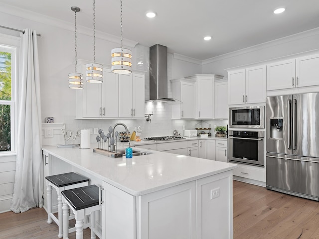 kitchen featuring appliances with stainless steel finishes, decorative light fixtures, white cabinetry, kitchen peninsula, and wall chimney exhaust hood