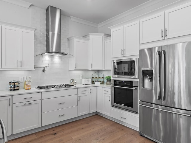 kitchen featuring wall chimney exhaust hood, white cabinetry, crown molding, tasteful backsplash, and appliances with stainless steel finishes