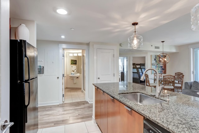 kitchen with pendant lighting, sink, light tile patterned floors, black refrigerator, and light stone counters