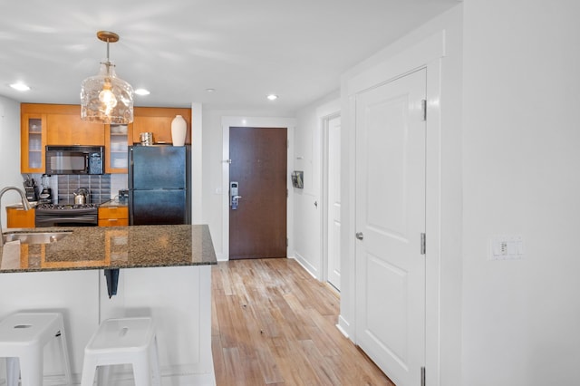 kitchen featuring sink, dark stone countertops, black appliances, a kitchen bar, and decorative light fixtures