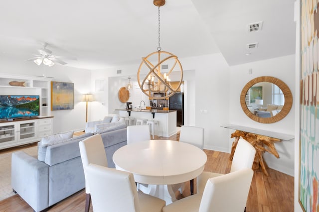 dining room featuring ceiling fan with notable chandelier and light hardwood / wood-style flooring