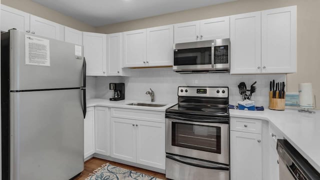 kitchen with sink, light wood-type flooring, appliances with stainless steel finishes, white cabinets, and backsplash