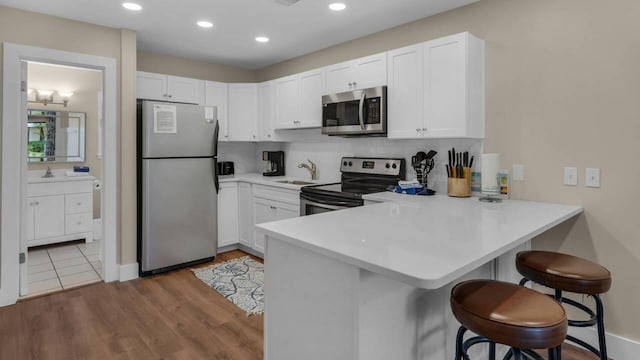 kitchen featuring a breakfast bar, appliances with stainless steel finishes, kitchen peninsula, and white cabinets