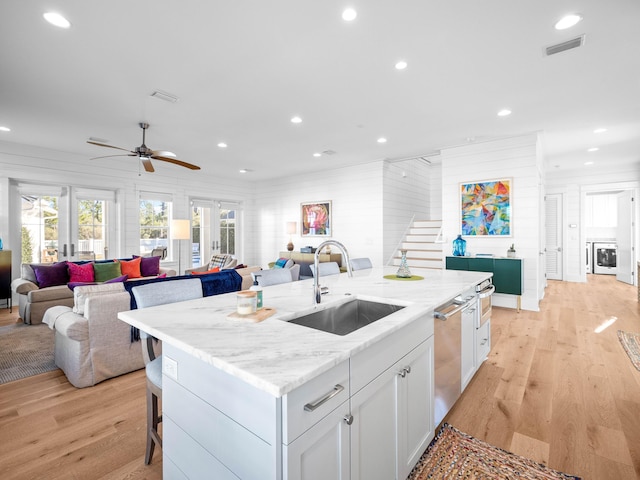 kitchen with sink, light stone counters, white cabinets, a center island with sink, and french doors