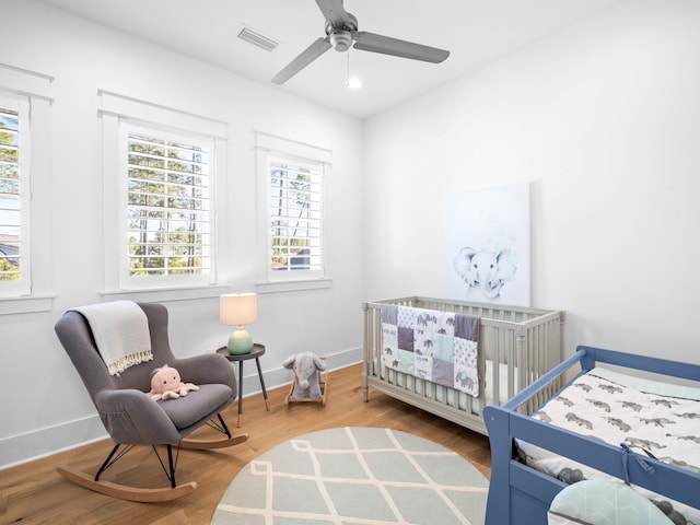 bedroom with a nursery area, ceiling fan, and wood-type flooring