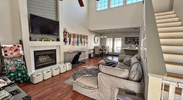 living room with ceiling fan, a towering ceiling, wood-type flooring, and a tiled fireplace