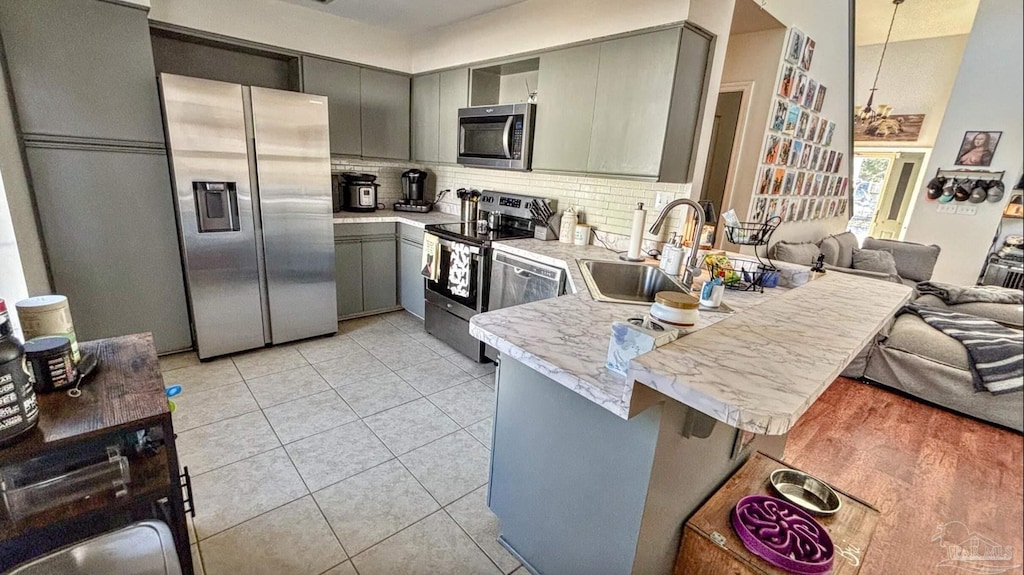 kitchen with sink, gray cabinetry, a kitchen breakfast bar, kitchen peninsula, and stainless steel appliances