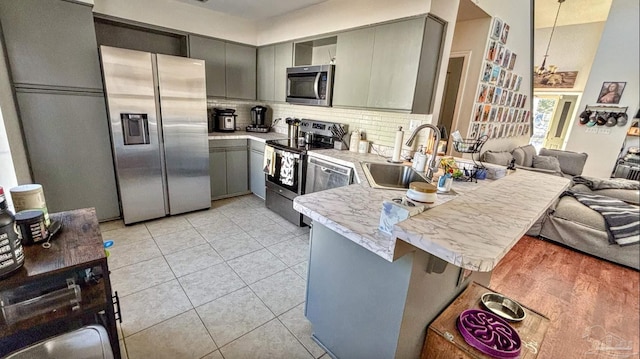 kitchen with sink, gray cabinetry, a kitchen breakfast bar, kitchen peninsula, and stainless steel appliances