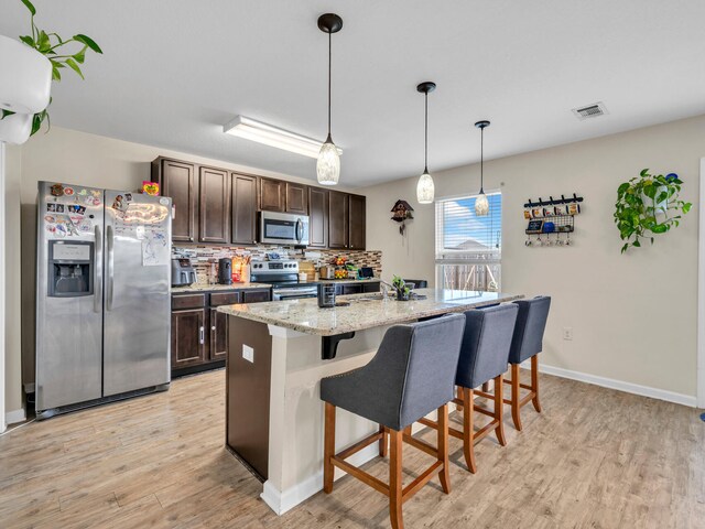 kitchen with a breakfast bar, tasteful backsplash, dark brown cabinets, an island with sink, and stainless steel appliances