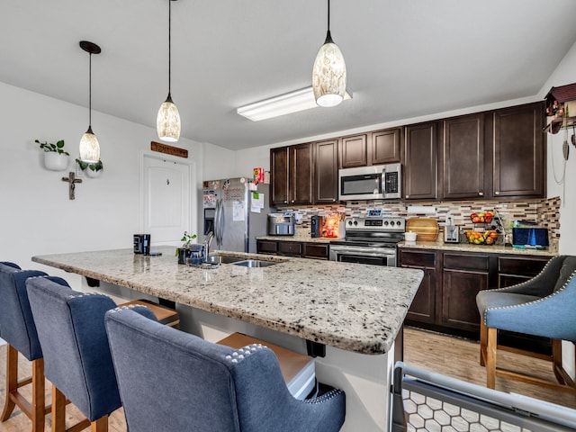 kitchen with dark brown cabinetry, decorative light fixtures, a kitchen breakfast bar, and appliances with stainless steel finishes