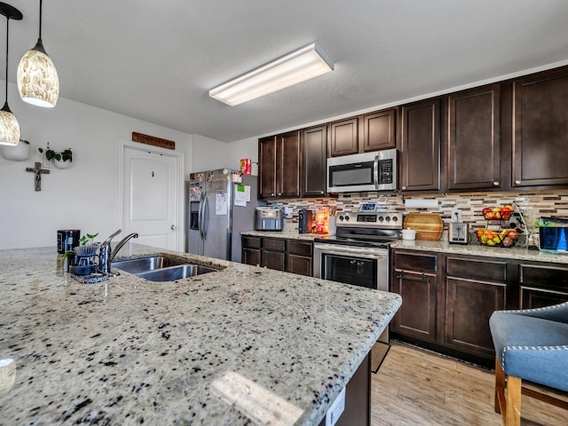 kitchen featuring sink, hanging light fixtures, appliances with stainless steel finishes, light stone countertops, and backsplash