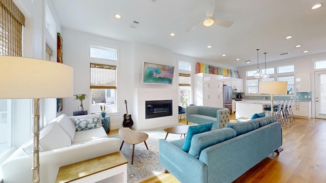 living room with ceiling fan, light hardwood / wood-style flooring, and a high ceiling