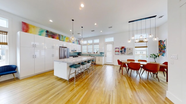 kitchen featuring white cabinetry, stainless steel fridge, a kitchen bar, hanging light fixtures, and a center island