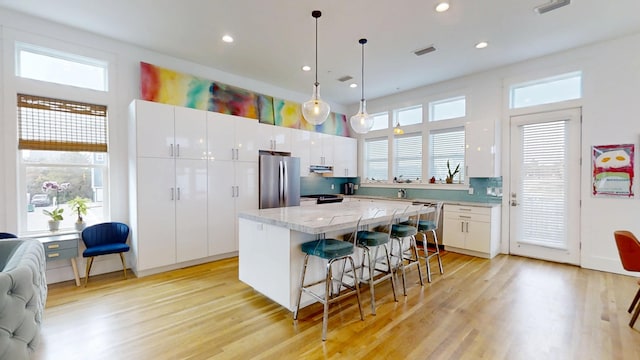 kitchen with stainless steel refrigerator, a kitchen breakfast bar, white cabinets, a kitchen island, and decorative light fixtures