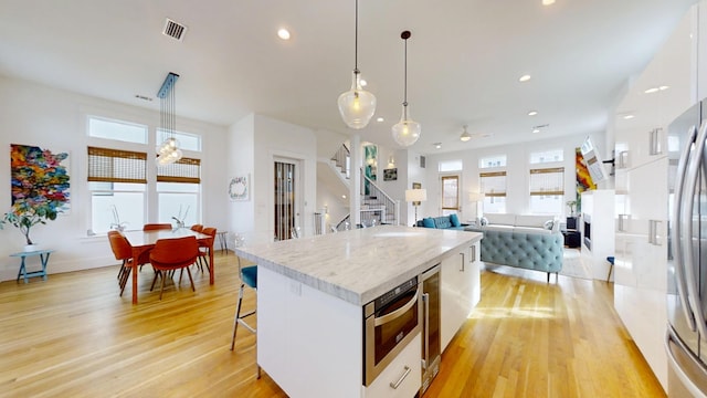 kitchen featuring a kitchen island, light wood-type flooring, hanging light fixtures, and white cabinets