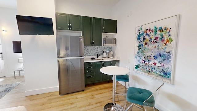 kitchen featuring sink, light hardwood / wood-style flooring, backsplash, stainless steel appliances, and green cabinetry