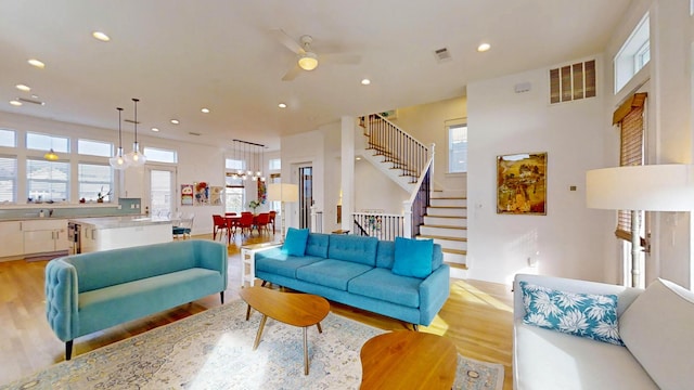 living room with ceiling fan with notable chandelier and light hardwood / wood-style flooring