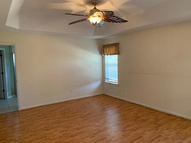 spare room with a tray ceiling, light hardwood / wood-style flooring, and ceiling fan