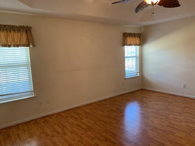 empty room with ceiling fan, wood-type flooring, and a raised ceiling