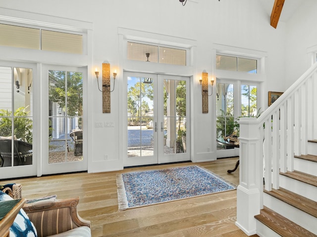 doorway featuring a high ceiling, french doors, stairway, light wood-type flooring, and beam ceiling