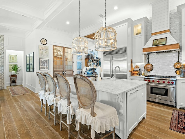 kitchen with premium range hood, premium appliances, a center island with sink, and white cabinets