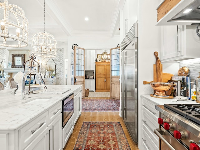 kitchen featuring built in appliances, wood finished floors, a sink, white cabinetry, and ornamental molding