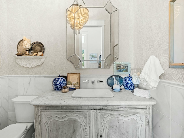 bathroom with toilet, wainscoting, vanity, and wallpapered walls