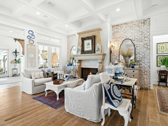 living area with a warm lit fireplace, light wood finished floors, coffered ceiling, and beam ceiling