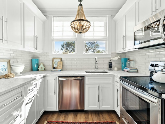 kitchen featuring decorative light fixtures, stainless steel appliances, white cabinets, a sink, and light stone countertops