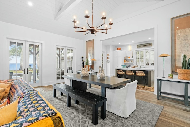 dining area with vaulted ceiling with beams, a chandelier, light hardwood / wood-style floors, and french doors