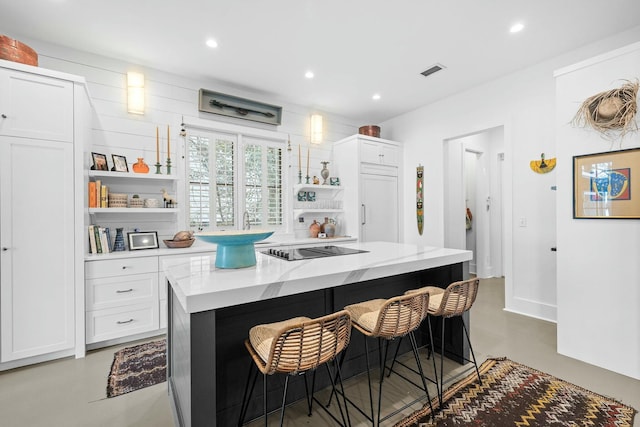 kitchen with a breakfast bar area, white cabinetry, a center island, black electric cooktop, and light stone countertops