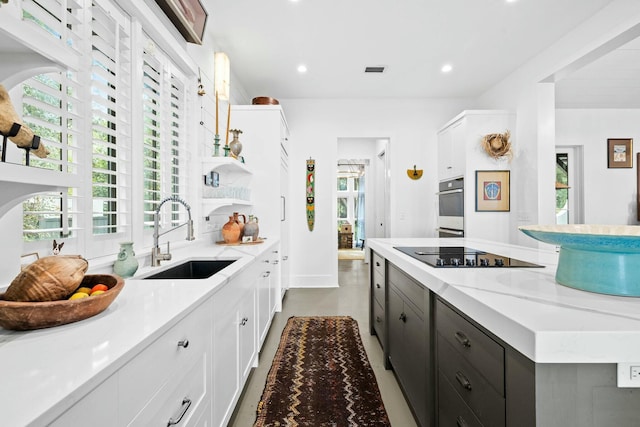 kitchen featuring sink, light stone counters, white cabinets, black electric cooktop, and stainless steel double oven