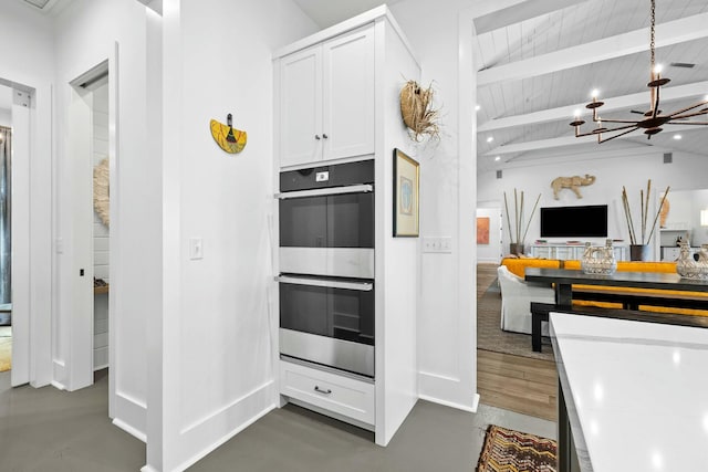 kitchen featuring stainless steel double oven, lofted ceiling with beams, white cabinets, wooden ceiling, and a chandelier