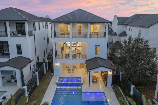 back of property at dusk with a fenced in pool, a patio, metal roof, an in ground hot tub, and a fenced backyard