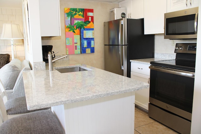 kitchen featuring stainless steel appliances, white cabinetry, a sink, and a peninsula