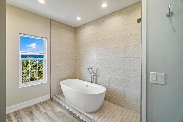 bathroom featuring a soaking tub, baseboards, wood finished floors, and recessed lighting