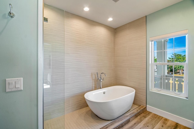 bathroom with baseboards, wood finished floors, walk in shower, a freestanding bath, and recessed lighting