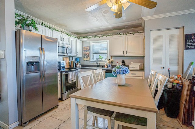 kitchen with light tile patterned flooring, sink, crown molding, stainless steel appliances, and white cabinets