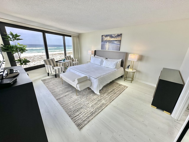 4045 Beachside One Dr # 4045, Miramar Beach, FL 32550 - bedroom with light wood-style floors, a textured ceiling, baseboards, and view of water and beach