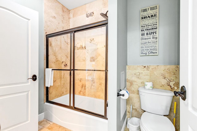 bathroom with toilet, combined bath / shower with glass door, and tile walls