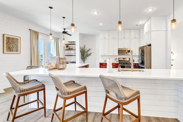 kitchen with appliances with stainless steel finishes, decorative light fixtures, white cabinetry, a breakfast bar area, and light hardwood / wood-style flooring