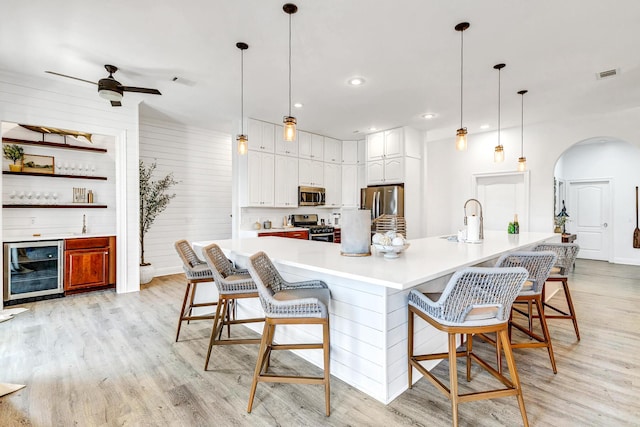 kitchen featuring pendant lighting, a breakfast bar area, white cabinets, stainless steel appliances, and light wood-type flooring