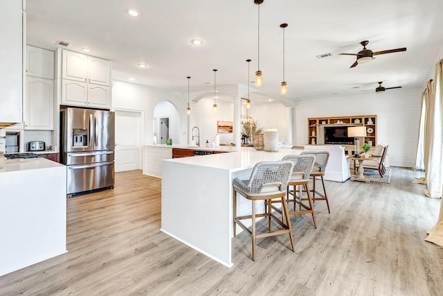 kitchen with stainless steel fridge, a breakfast bar area, white cabinetry, light hardwood / wood-style floors, and decorative light fixtures