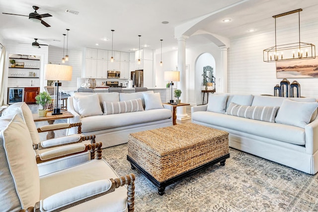 living room featuring ornate columns, wooden walls, and ceiling fan