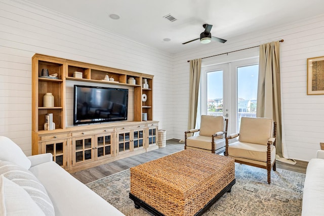 living room with wooden walls, hardwood / wood-style floors, ceiling fan, and french doors