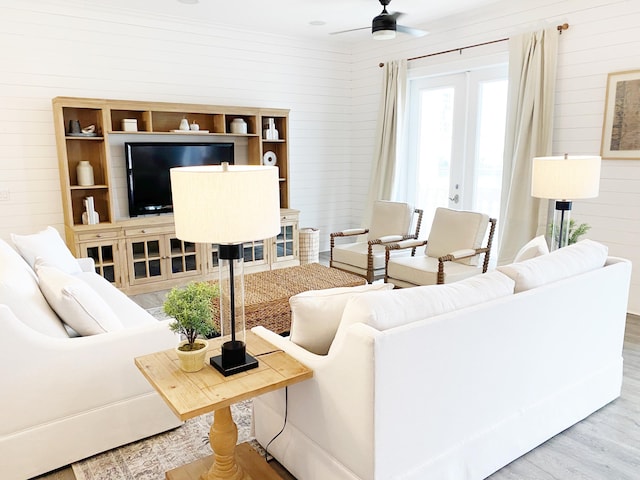 living room with hardwood / wood-style flooring, ceiling fan, wooden walls, and french doors