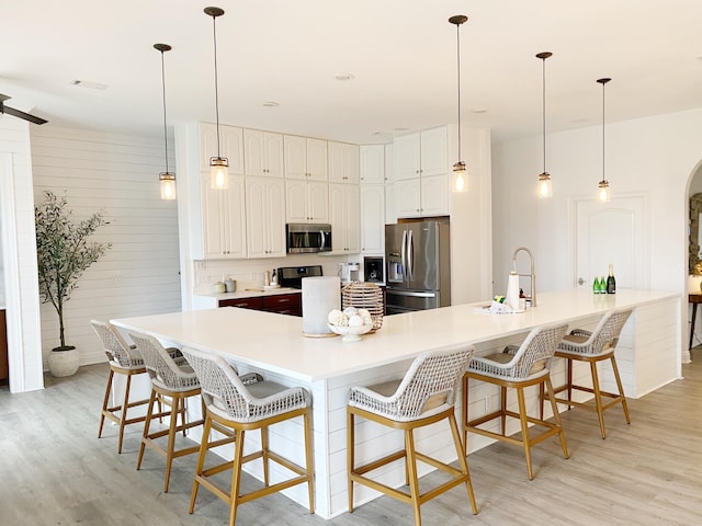 kitchen featuring stainless steel appliances, pendant lighting, white cabinets, and a kitchen bar